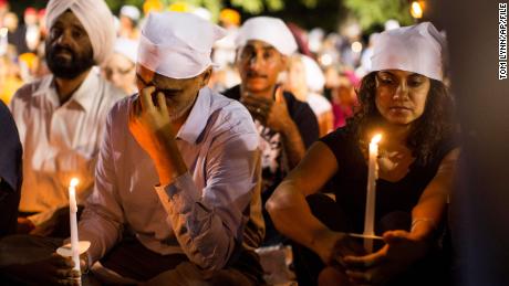 FILE - In this Aug. 7, 2012 file photo, people cover their heads at a candle light vigil in Oak Creek, Wis., for the victims of a mass shooting at the Sikh Temple of Wisconsin on Sunday. Wade Michael Page, the man who killed six Sikh worshippers before fatally shooting himself had a history of alcohol problems and underwent a noticeable personality change in the preceding year, according to an investigative report released Tuesday, Aug. 28, 2012. (AP Photo/Tom Lynn, File)