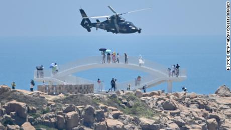 Tourists look on as a Chinese military helicopter flies past Pingtan island, one of mainland China&#39;s closest point from Taiwan, in Fujian province on August 4, 2022, ahead of massive military drills off Taiwan following US House Speaker Nancy Pelosi&#39;s visit to the self-ruled island. - China is due on August 4 to kick off its largest-ever military exercises encircling Taiwan, in a show of force straddling vital international shipping lanes following a visit to the self-ruled island by US House Speaker Nancy Pelosi. (Photo by Hector RETAMAL / AFP) (Photo by HECTOR RETAMAL/AFP via Getty Images)