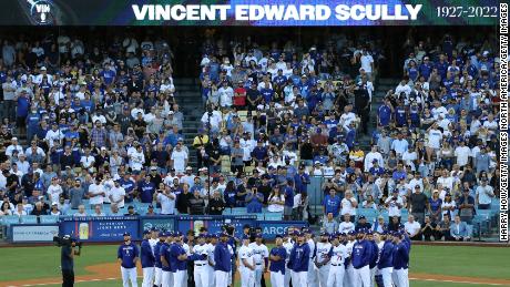 Los jugadores y entrenadores de los Dodgers de Los Ángeles se paran en el campo mientras Vin Scully es honrado durante una ceremonia de juego.