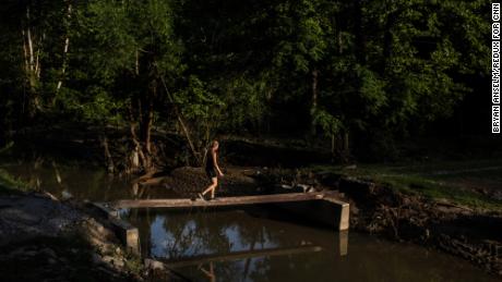 Volunteer Maris Hovee walks across a makeshift bridge after the roadway was washed away by floodwaters in Pine Top.