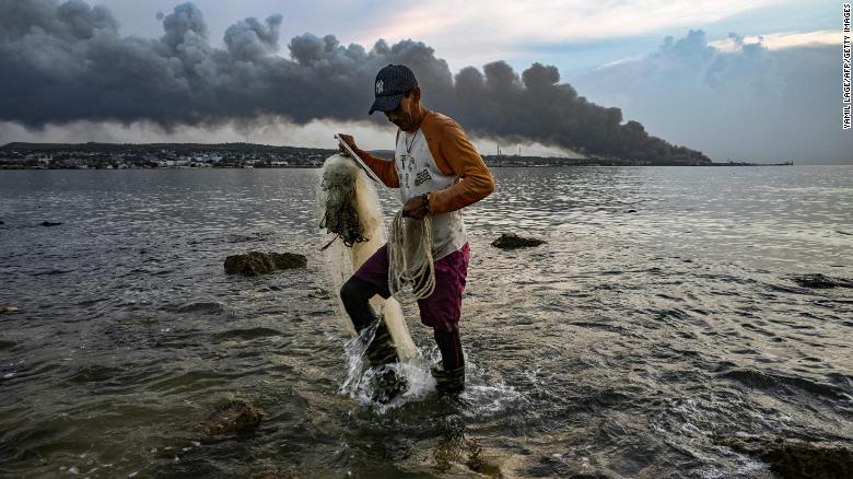 A man fishes as smoke rises from the massive fire at a fuel depot in Matanzas, Cuba, on August 9, 2022.