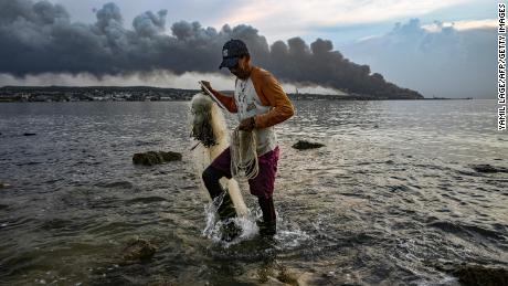 9 Ağustos 2022'de Küba'nın Matanzas kentindeki bir yakıt depolama tesisinde çıkan büyük yangından duman yükselirken bir adam balık tutuyor.