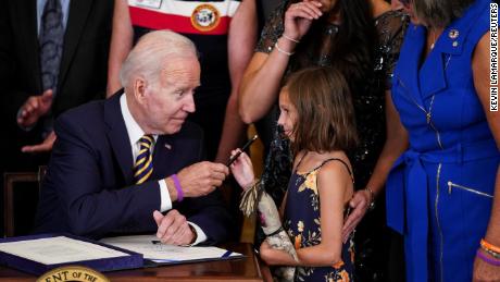 US President Joe Biden gives a pen to Brielle Robinson, the daughter of a sergeant.  1st Class Heath Robinson as her mother, Danielle Robinson, at a signing ceremony for 