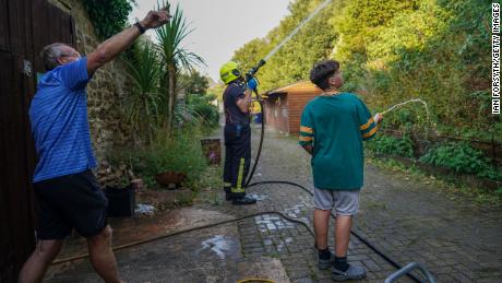 2022年8月11日、イギリスのスケルトンでは、地元住民が庭のホースを使って農地を掃除し、地元住宅を脅かした農作物の火災を鎮圧する消防隊員を支援します。 