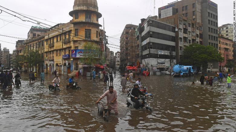 25 جولائی کو کراچی میں مون سون کی شدید بارشوں کے بعد لوگ سیلاب سے بھری ہوئی گلی سے گزر رہے ہیں۔