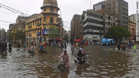 Mensen slenteren op een overstroomde straat na zware moessonregens in Karachi op 25 juli.