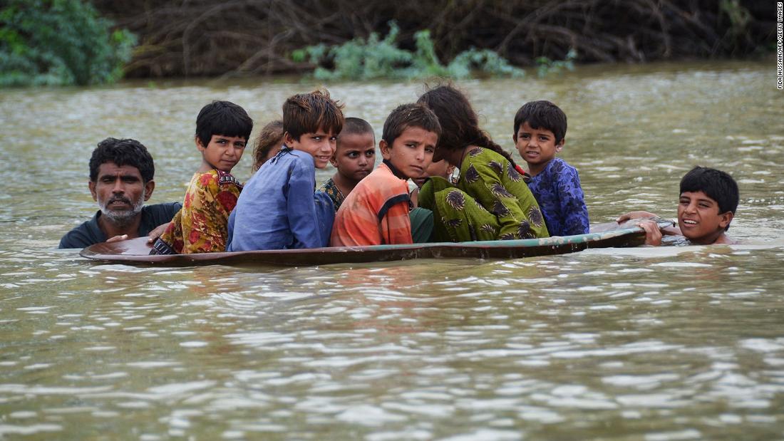 A man helps children navigate floodwaters using a satellite dish in Balochistan, Pakistan, on Friday, August 26.