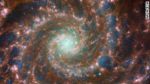 M74 shines at its brightest in this combined optical/mid-infrared image, featuring data from both the NASA/ESA Hubble Space Telescope and the NASA/ESA/CSA James Webb Space Telescope. The dust threaded through the arms of the galaxy is coloured red, and the young stars throughout the arms and the nuclear core are picked out in blue, by the James Webb Space Telescope&#39;s Mid-InfraRed Instrument -- MIRI. Meanwhile, the Hubble Space Telescope&#39;s Advanced Camera for Surveys adds depth: the glow of the heavier, older stars towards the galaxy&#39;s centre are primarily yellow, combined with the blue in this image to make a spooky green glow. The red bubbles of star formation are also visible in Hubble&#39;s optical wavelengths. Scientists combine data from telescopes operating across the electromagnetic spectrum to truly understand astronomical objects. In this way, data from Hubble and Webb compliment each other to provide a comprehensive view of the spectacular M74 galaxy. Links Image A Image C 