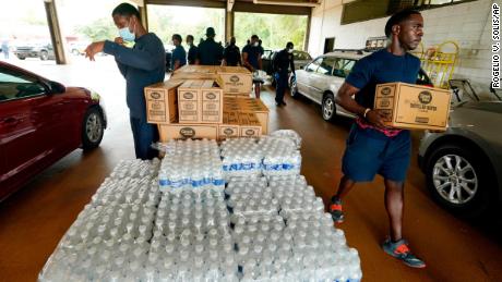 Firefighters and recruits for the Jackson Fire Department carry cases of bottled water to residents vehicles, August 18, 2022, as part of the city&#39;s response to longstanding water system problems. 