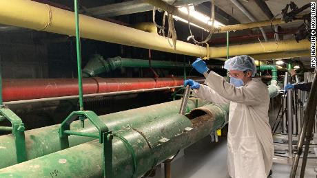 Queens College Research Assistant Justin Silbiger collects a wastewater sample from a sewage pipe in the basement of NYC Health + Hospitals/Elmhurst. 