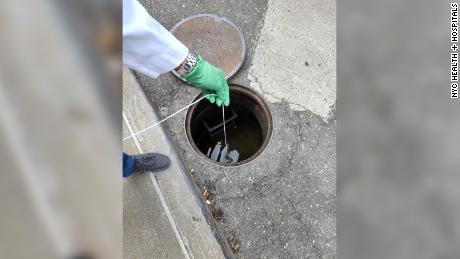Queens College Research Assistant Sherin Kannoly collects a wastewater sample from a manhole on the grounds of NYC Health + Hospitals/Queens.