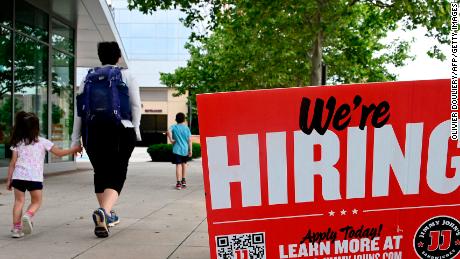 People walk past a &quot;now hiring&quot; sign posted outside of a restaurant in Arlington, Virginia. 