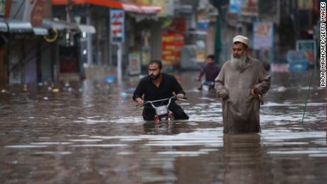 Men are pushed across a water-filled street after the monsoon rains in Rawalpindi, Pakistan, on July 13, 2022. 