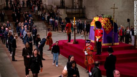 Members of the public view the Queen&#39;s coffin, which is draped with the Royal Standard, on which lie the Instruments of State -- the Imperial State Crown and the Orb and Sceptre. 