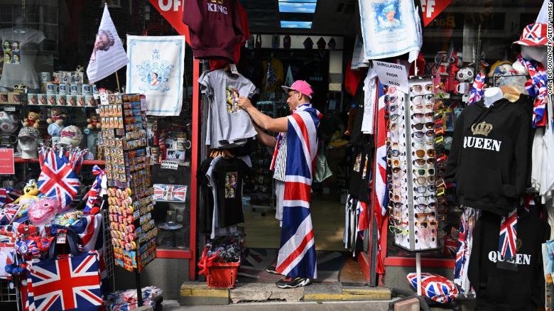 A man draped in a Union Jack flag browses Queen paraphernalia at a souvenir shop in Windsor.
