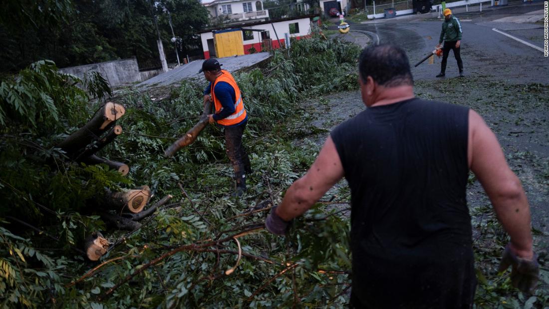 People clear a road from a fallen tree in Yauco, Puerto Rico, on Sunday.