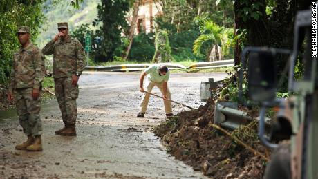 Национальная гвардия регулирует движение в Кайе, Пуэрто-Рико, где житель Луис Ногейра помогает расчищать дорогу.