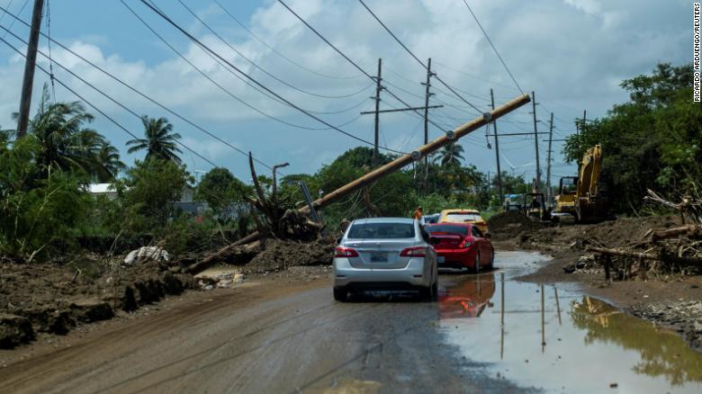 Cars drive Wednesday under a downed power pole in Santa Isabel, Puerto Rico.