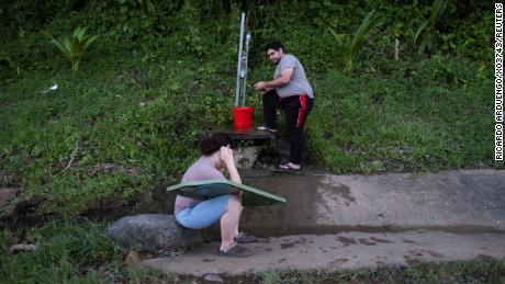 Ein Mann sammelt am Mittwoch nach dem Hurrikan Fiona in Cayey, Puerto Rico, Wasser aus einer Quelle auf einem Berg am Straßenrand