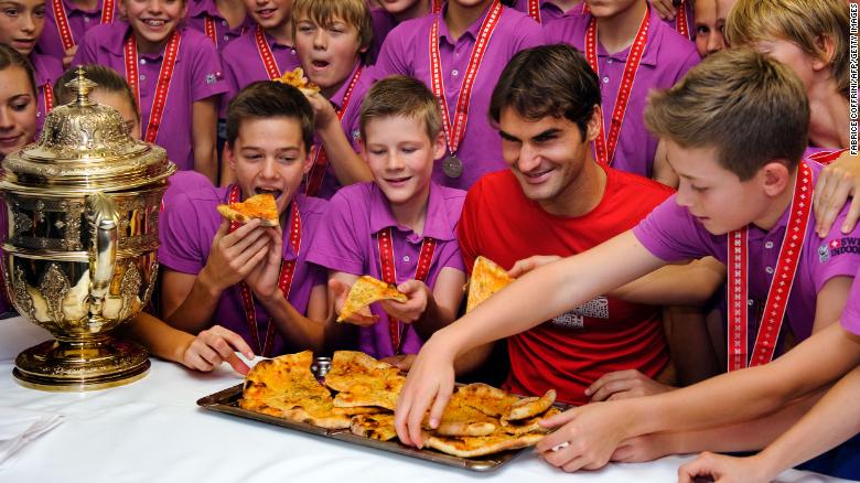 After winning a tournament in Switzerland, Federer poses with ball boys and girls as they pick up slices of pizza in 2011. Federer, who once worked as a ball boy in Basel, hosted the pizza party.