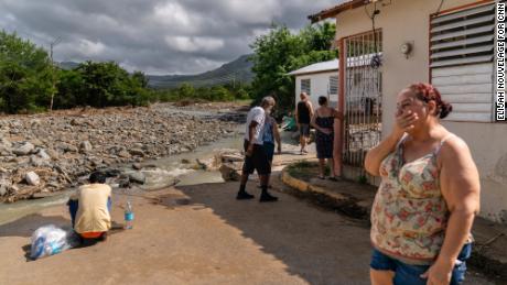 Carmen Baez becomes emotional while standing in front of where her home used to be as a boy uses her washing machine valves to collect fresh water in Guayama.