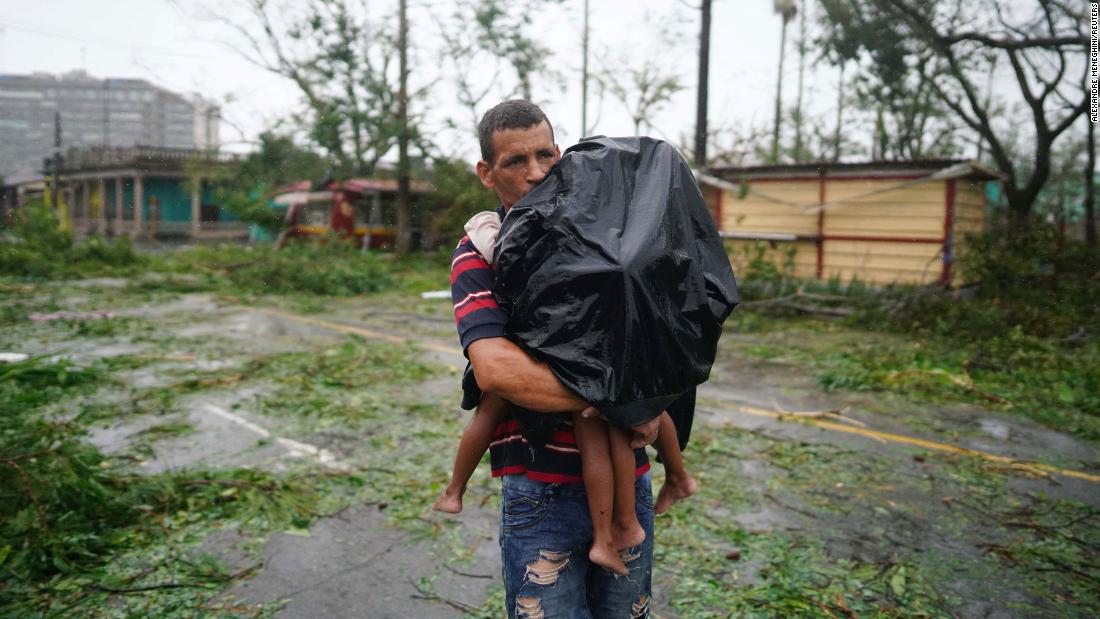 A man carries his children through rain and debris in Pinar del Rio on Tuesday.