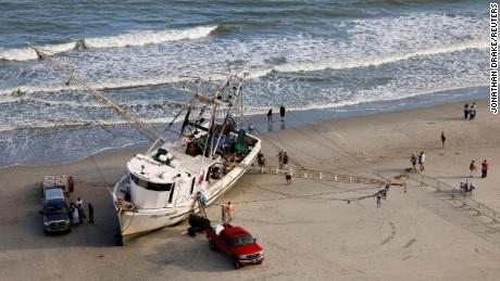 Workers and owners of a large shrimping boat prepare their vessel for towing back into the water Saturday after it was swept ashore in Myrtle Beach, South Carolina.