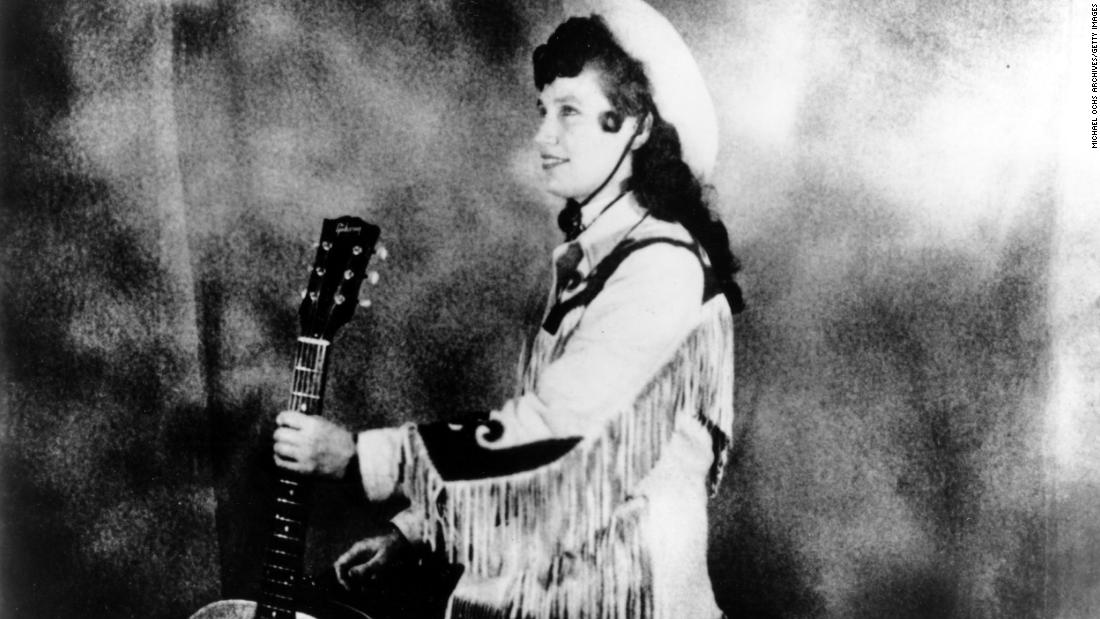 Lynn wears a cowboy hat and a fringe western style jacket while holding an acoustic guitar in Nashville circa 1960. 