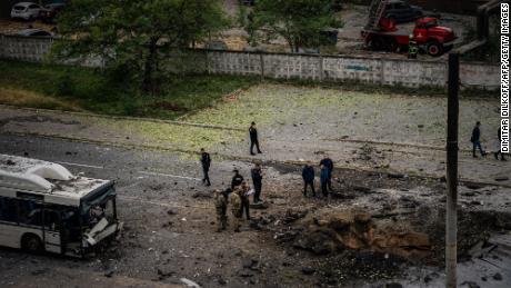 Investigators examine a crater next to a damaged bus following a missile strike in Dnipro on Monday.