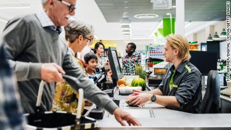 A cashier ringing up a senior couple&#39;s groceries so they can pay at their local supermarket.