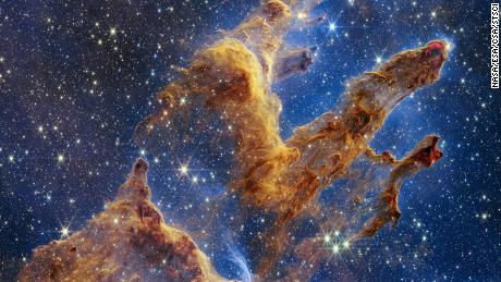 The Pillars of Creation are set off in a kaleidoscope of colour in the NASA/ESA/CSA James Webb Space Telescope&#39;s near-infrared-light view. The pillars look like arches and spires rising out of a desert landscape, but are filled with semi-transparent gas and dust, and ever changing. This is a region where young stars are forming -- or have barely burst from their dusty cocoons as they continue to form. Protostars are the scene-stealers in this Near-Infrared Camera (NIRCam) image. These are the bright red orbs that sometimes appear with eight diffraction spikes. When knots with sufficient mass form within the pillars, they begin to collapse under their own gravity, slowly heat up, and eventually begin shining brightly. Along the edges of the pillars are wavy lines that look like lava. These are ejections from stars that are still forming. Young stars periodically shoot out jets that can interact within clouds of material, like these thick pillars of gas and dust. This sometimes also results in bow shocks, which can form wavy patterns like a boat does as it moves through water. These young stars are estimated to be only a few hundred thousand years old, and will continue to form for millions of years. Although it may appear that near-infrared light has allowed Webb to &quot;pierce through&quot; the background to reveal great cosmic distances beyond the pillars, the interstellar medium stands in the way, like a drawn curtain. This is also the reason why there are no distant galaxies in this view. This translucent layer of gas blocks our view of the deeper universe. Plus, dust is lit up by the collective light from the packed &quot;party&quot; of stars that have burst free from the pillars. It&#39;s like standing in a well-lit room looking out a window -- the interior light reflects on the pane, obscuring the scene outside and, in turn, illuminating the activity at the party inside. Webb&#39;s new view of the Pillars of Creation will help researchers revamp models of star formation.