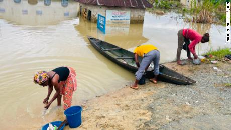Chigozie Uzo (L), a displaced resident of Odi, in Nigeria&#39;s southern Bayelsa State rinses her uncooked fish in dirty floodwater, Tuesday.