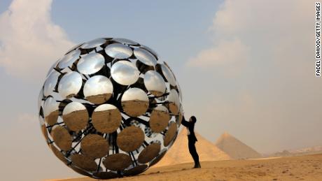 Visitors pose by the &quot;Orb: Under the same Sun&quot; installation by Madrid-based international artist SpY at the Giza pyramids necropolis during the second edition of the Art D&#39;Égypte exhibition &quot;Forever is Now&quot; on October 27 in Giza, Egypt. 