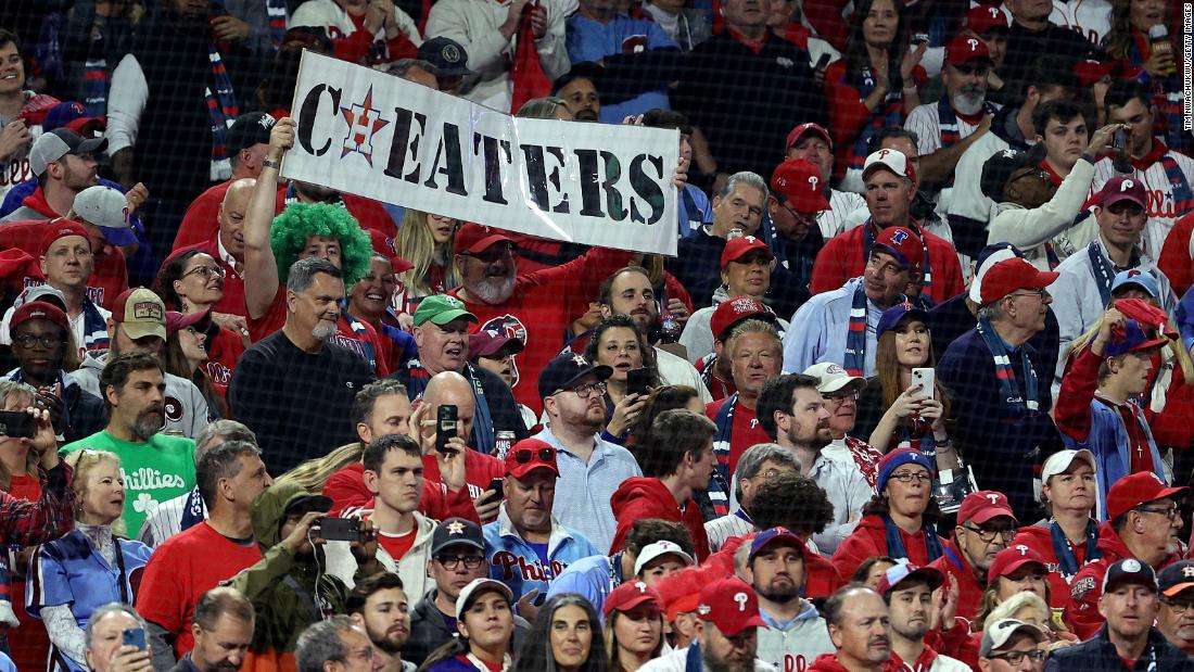 Phillies fans hold up a &quot;cheaters&quot; sign with the Astros&#39; logo on Tuesday night. The Astros won the World Series in 2017, but many baseball fans consider that title tainted because of a cheating scandal. Major League Baseball found that the team had illegally created a system that decoded and communicated the opposing teams&#39; pitching signs during their championship season, leading Astros owner and chairman Jim Crane to fire manager AJ Hinch and general manager Jeff Luhnow.