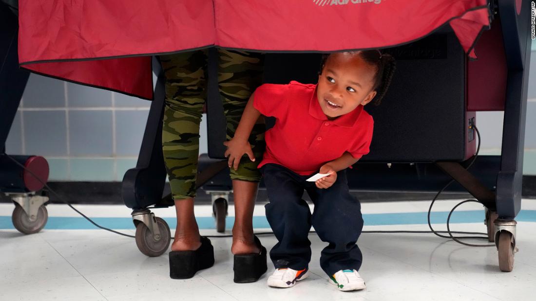 Kash Strong, 3, peeks out from under the curtain of a voting booth as his mother, Sophia Amacker, casts her vote in New Orleans.