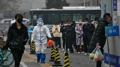A worker in a protective suit sprays disinfectant as residents stand in line for their routine Covid-19 tests at a coronavirus testing site in Beijing on Thursday, November 24, 2022. 
