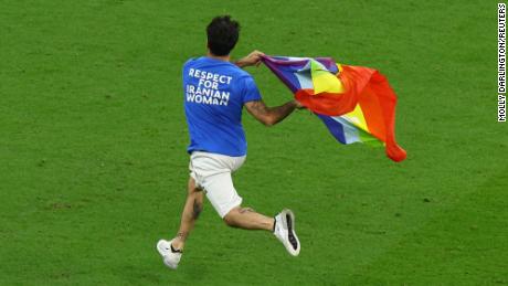 A pitch invader runs onto the pitch wearing a t-shirt with a message saying: &#39;Respect for Iranian Woman&#39; on the back and holding a rainbow flag.