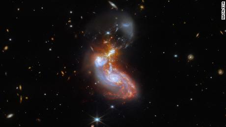 A merging galaxy pair cavort in this image captured by the NASA/ESA/CSA James Webb Space Telescope. This pair of galaxies, known to astronomers as II ZW 96, is roughly 500 million light-years from Earth and lies in the constellation Delphinus, close to the celestial equator. As well as the wild swirl of the merging galaxies, a menagerie of background galaxies are dotted throughout the image.The two galaxies are in the process of merging and as a result have a chaotic, disturbed shape. The bright cores of the two galaxies are connected by bright tendrils of star-forming regions, and the spiral arms of the lower galaxy have been twisted out of shape by the gravitational perturbation of the galaxy merger. It is these star-forming regions that made II ZW 96 such a tempting target for Webb; the galaxy pair is particularly bright at infrared wavelengths thanks to the presence of the star formation. This observation is from a collection of Webb measurements delving into the details of galactic evolution, in particular in nearby Luminous Infrared Galaxies such as II ZW 96. These galaxies, as the name suggests, are particularly bright at infrared wavelengths, with luminosities more than 100 billion times that of the Sun. An international team of astronomers proposed a study of complex galactic ecosystems — including the merging galaxies in II ZW 96 — to put Webb through its paces soon after the telescope was commissioned. Their chosen targets have already been observed with ground-based telescopes and the NASA/ESA Hubble Space Telescope, which will provide astronomers with insights into Webb&#39;s ability to unravel the details of complex galactic environments. Webb captured this merging galaxy pair with a pair of its cutting-edge instruments; NIRCam — the Near-InfraRed Camera — and MIRI, the Mid-InfraRed Instrument. If you are interested in exploring the differences between Hubble and Webb&#39;s observations of II ZW 96, you can do so here.MIRI was contributed by ESA an