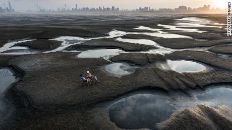 TOPSHOT - This photo taken on September 2, 2022 shows people sitting on a section of a parched river bed along the Yangtze River in Wuhan in China&#39;s central Hubei province. - China OUT (Photo by AFP) / China OUT (Photo by STR/AFP via Getty Images)