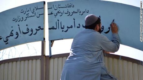 A member of the Taliban replaces a sign of the Department for Women&#39;s Affairs with one of the Ministry for the Promotion of Virtue and Prevention of Vice at a government building in Kandahar, Afghanistan, in October 2021.