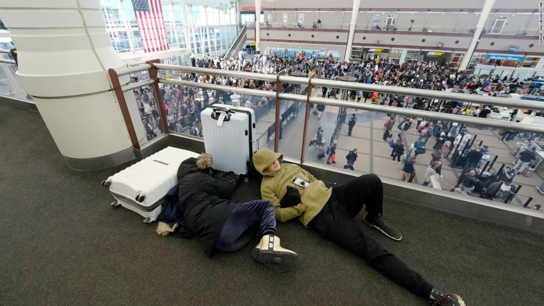 Travelers sleep while lines of people pass through a security checkpoint at Denver International Airport.
