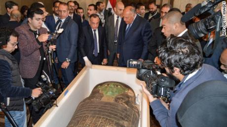 Egyptian Foreign Minister Sameh Shoukry and head of Egypt&#39;s Supreme Council of Antiquities Mostafa Waziri are surrounded by journalists as they inspect a wooden sarcophagus, which was handed over by the US in a ceremony on Monday in Cairo, Egypt.  