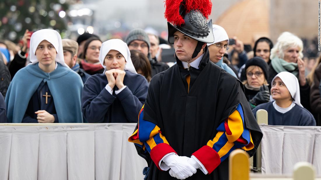 Mourners attend the public funeral mass for Pope Emeritus Benedict XVI in St. Peter&#39;s Square, preceded by a member of the Pontifical Swiss Guard. 