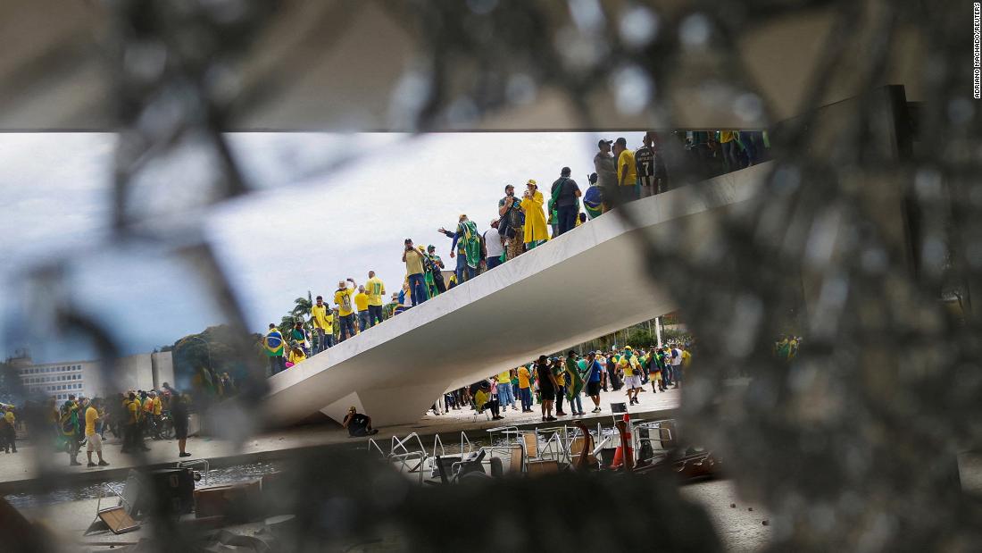 Supporters of former President Jair Bolsonaro are pictured through broken glass as they hold a demonstration.