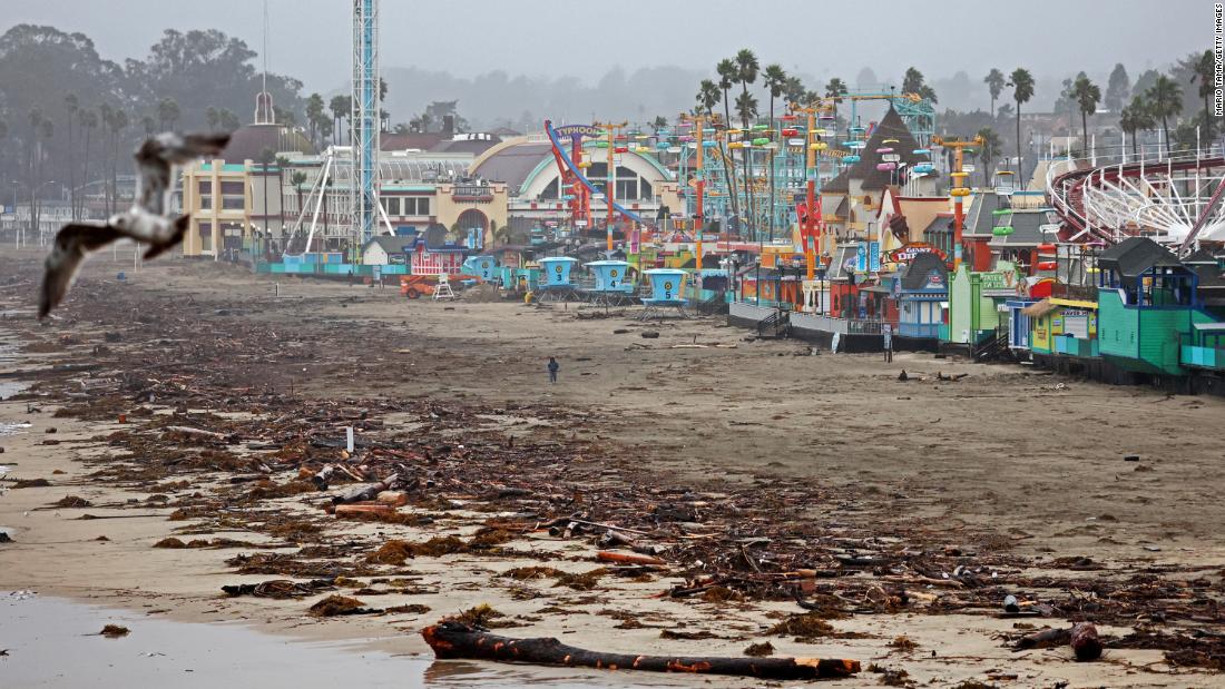 A person walks near driftwood and storm debris that washed up in front of the Santa Cruz Beach Boardwalk amusement park.