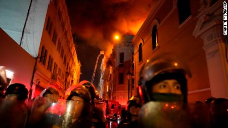 Police in riot gear block a street as a building burns behind them in Lima, Peru, Thursday.