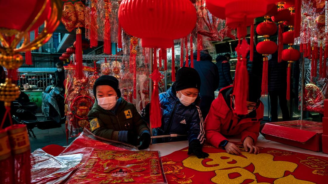 Children wear masks as they look at a large banner with the character Fu or luck as they shop for decorations for Lunar New Year at a street vendor on January 21, in Beijing, China.