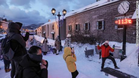 Tourists pose for photos in front of a thermometer reading -11.3 degrees Celsius (11.6 F), in Otaru, Hokkaido prefecture of northern Japan on January 24, 2023.