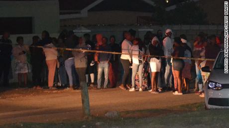 Bystanders wait behind a police tape marking the scene of a mass shooting in Gqeberha, South Africa, on January 29, 2023. - Gunmen opened fire on a group of people celebrating a birthday at the weekend in a township in South Africa, killing eight and wounding three others, police said Monday.The birthday celebrant was among those gunned down in the mass shooting in the southern port city of Gqeberha, formerly Port Elizabeth. (Photo by Luvuyo Mehlwana / AFP) (Photo by LUVUYO MEHLWANA/AFP via Getty Images)