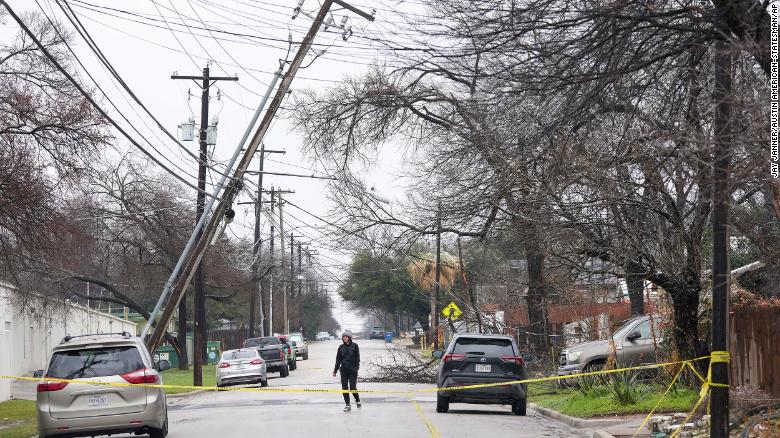Haley Samford walks past a leaning utility pole Thursday in Austin, Texas, after an ice storm covered tree branches and power lines with ice.